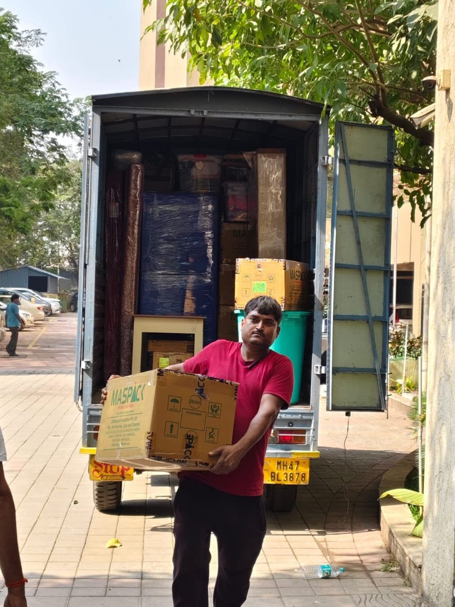 A Shifter worker carrying a packed carton to a loaded moving tempo outside a building